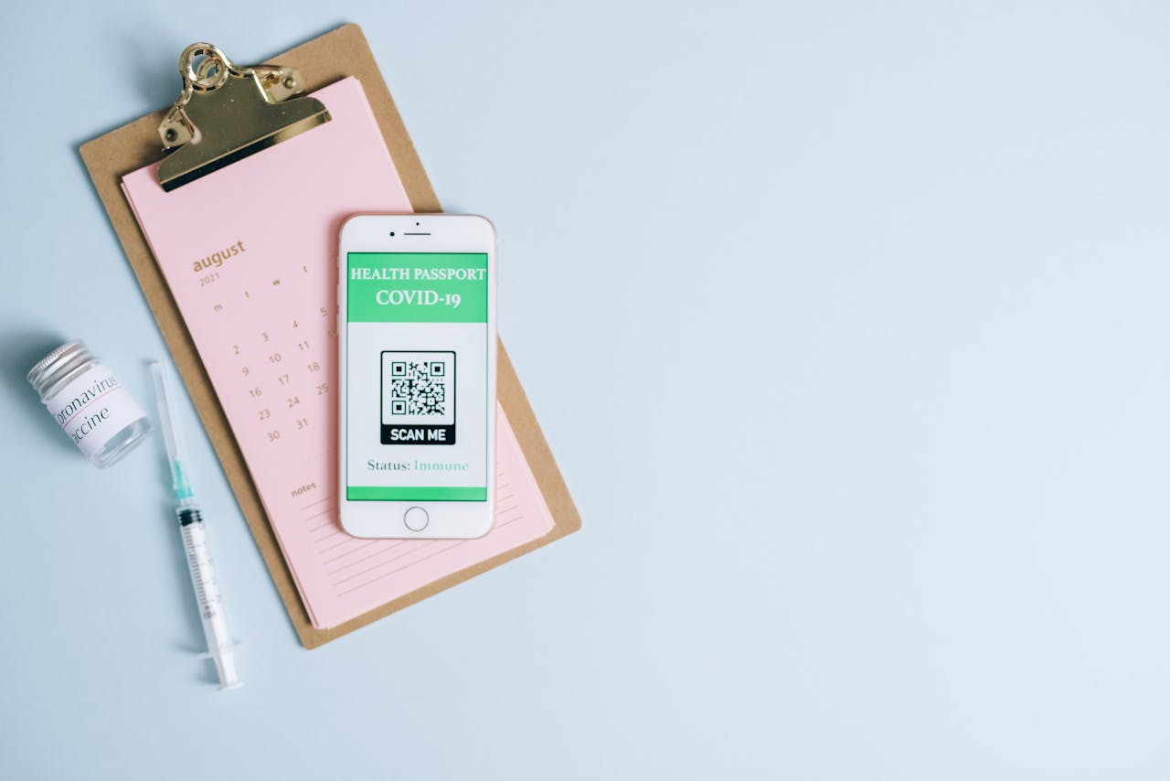 Flat lay image of COVID-19 health passport on a smartphone alongside a syringe and vaccine vial.